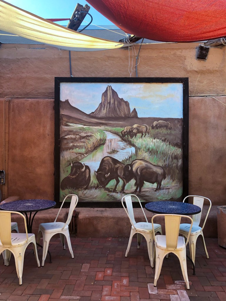 outdoor seating area in Albuquerque, NM with a painting of Bison grazing in the background