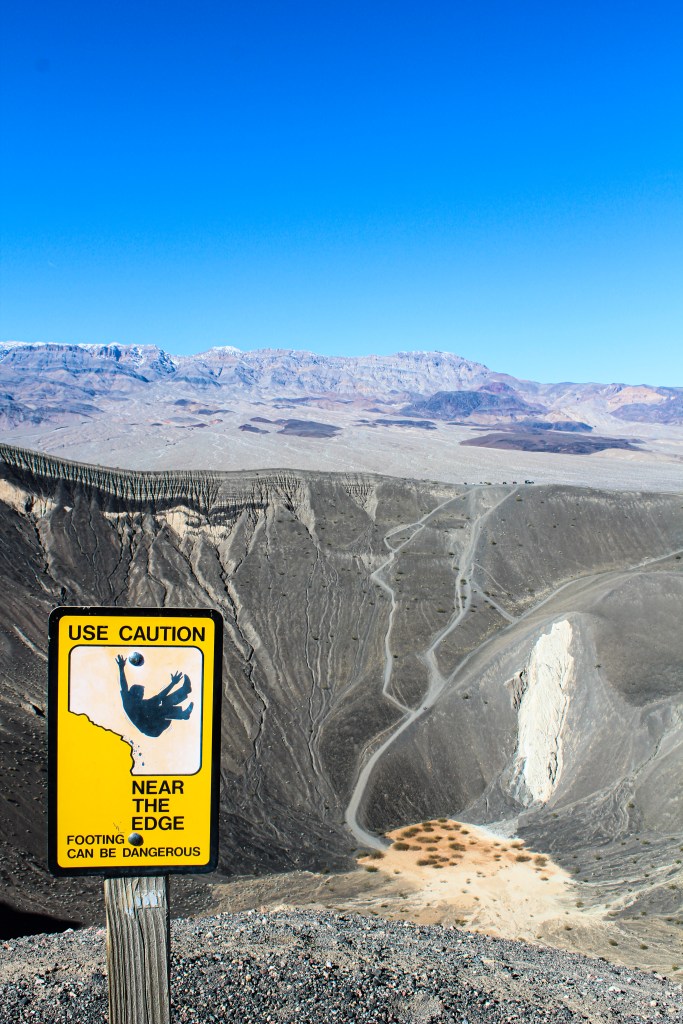 Sign saying use caution, near the edge footing can be dangerous posted near the edge of Ubehebe Crater 
